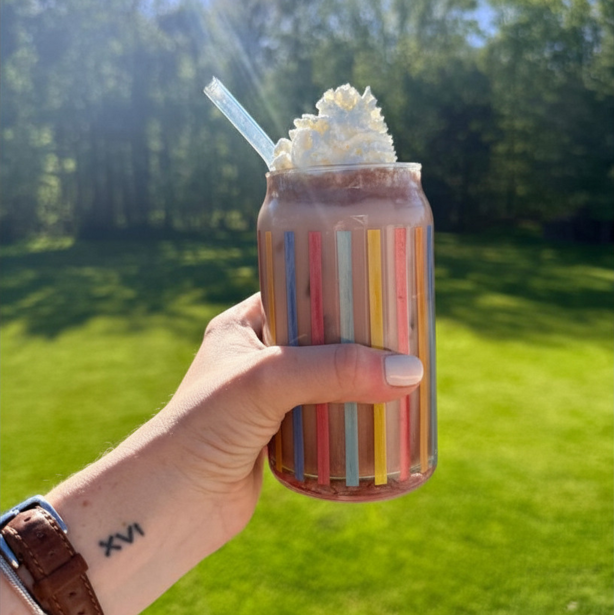 Hand holding a striped glass of iced cocoa topped with whipped cream outdoors